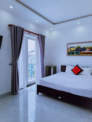 A modern hotel room with a large bed, a painting on the wall, and a balcony with curtains. - Blue Fish Villa (Da Nang)