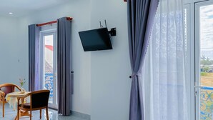 A hotel room with a bed, a TV mounted on the wall, a dining table with chairs, and a view of the outdoors through the window. - Blue Fish Villa (Da Nang)