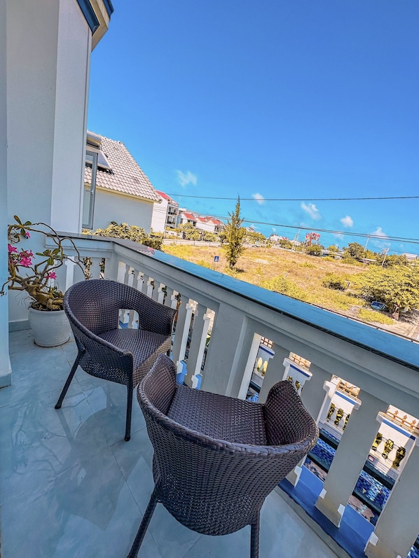 A balcony with two wicker chairs, a potted plant, and a view of a residential area with houses and a clear sky. - Blue Fish Villa (Da Nang)