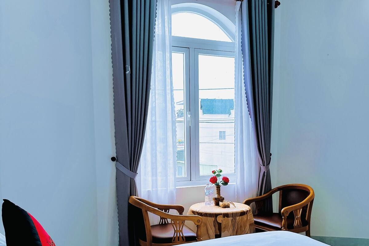 A hotel room with a bed, a small table with chairs, and a window with curtains.