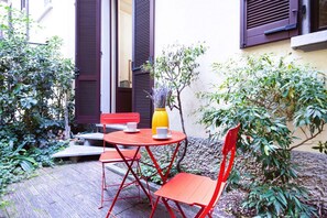 A small outdoor seating area with a red metal table and chairs, a yellow vase with flowers, and a potted plant. - Easylife - Prestigious apartment in Risorgimento (Milano)