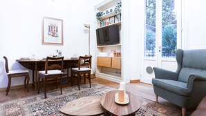 A living room with a dining area, a television on a shelf, and a large window. - Easylife - Prestigious apartment in Risorgimento (Milano)