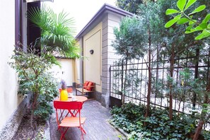 A small patio with a red table and chairs, surrounded by plants and a fence. - Easylife - Prestigious apartment in Risorgimento (Milano)