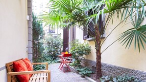 A narrow courtyard with a wooden bench, a red chair, and a small table. - Easylife - Prestigious apartment in Risorgimento (Milano)