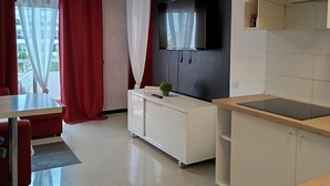 Eine moderne Küche mit Flachbildfernseher, einem Essbereich mit Tisch und Stühlen sowie einer kleinen Pflanze auf der Arbeitsplatte.