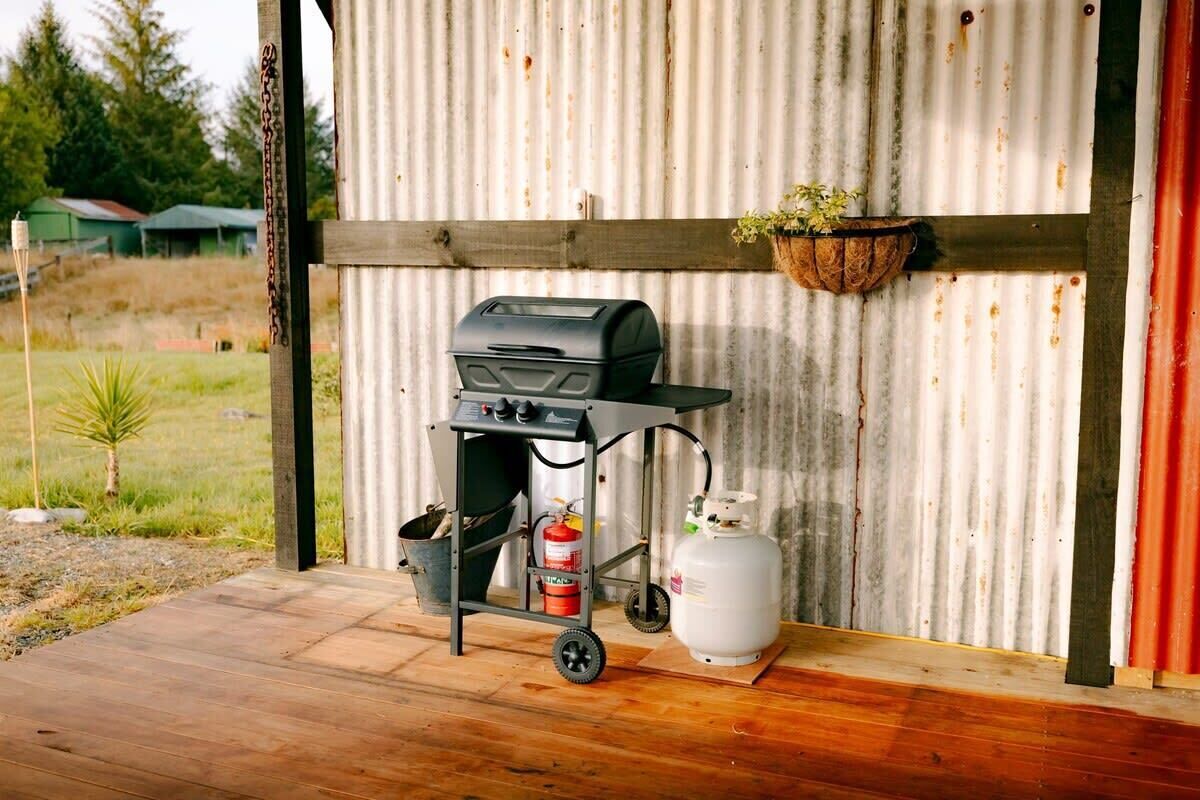 A portable grill with a gas tank and a fire extinguisher on a wooden deck.
