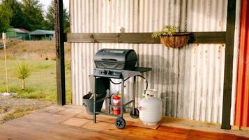 A portable grill with a gas tank and a fire extinguisher on a wooden deck.