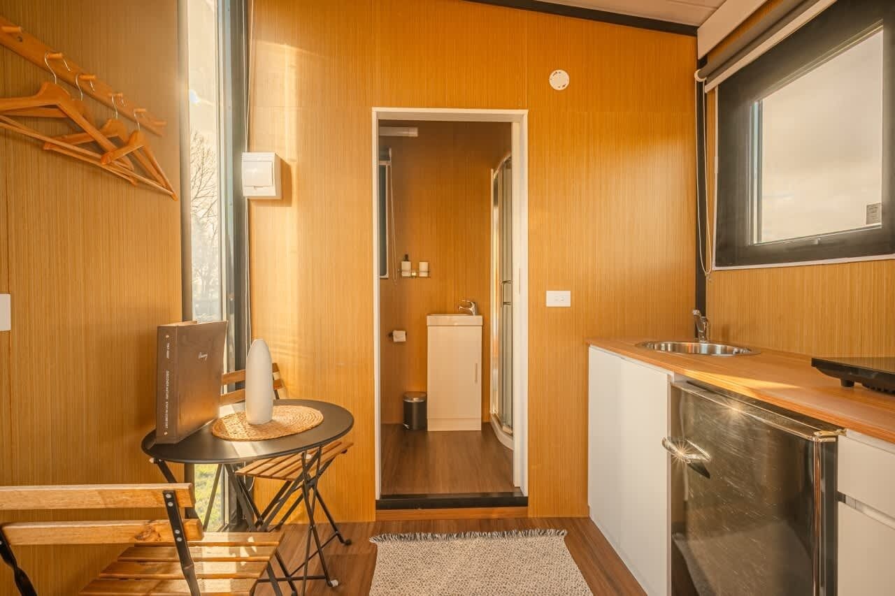 Eine kompakte Küche mit Spüle, ein kleiner Essbereich mit Tisch und Stühlen sowie eine Holzwand mit Kleiderhaken.