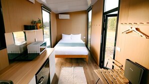 A compact room with a bed, a desk with a microwave, a laptop, and a bench.