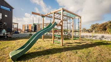 Ein Spielplatz mit Rutsche und Klettergerüsten, vor einer Bebauung und Bäumen.