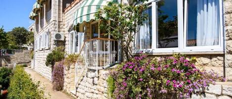 Un bâtiment en pierre doté d’un balcon, d’une fenêtre avec des rideaux et de plantes en fleurs.