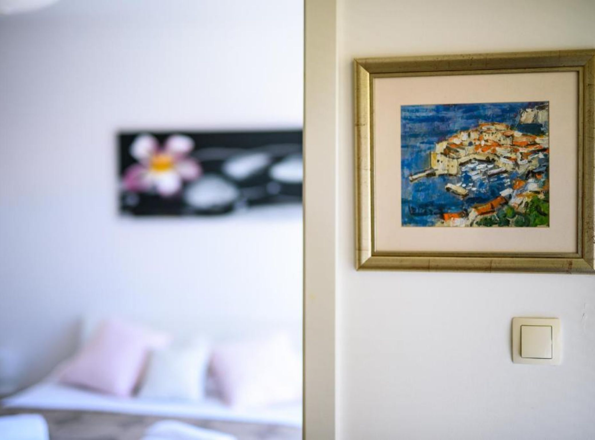Et værelse med en seng, et indrammet billede og en stikkontakt på væggen.