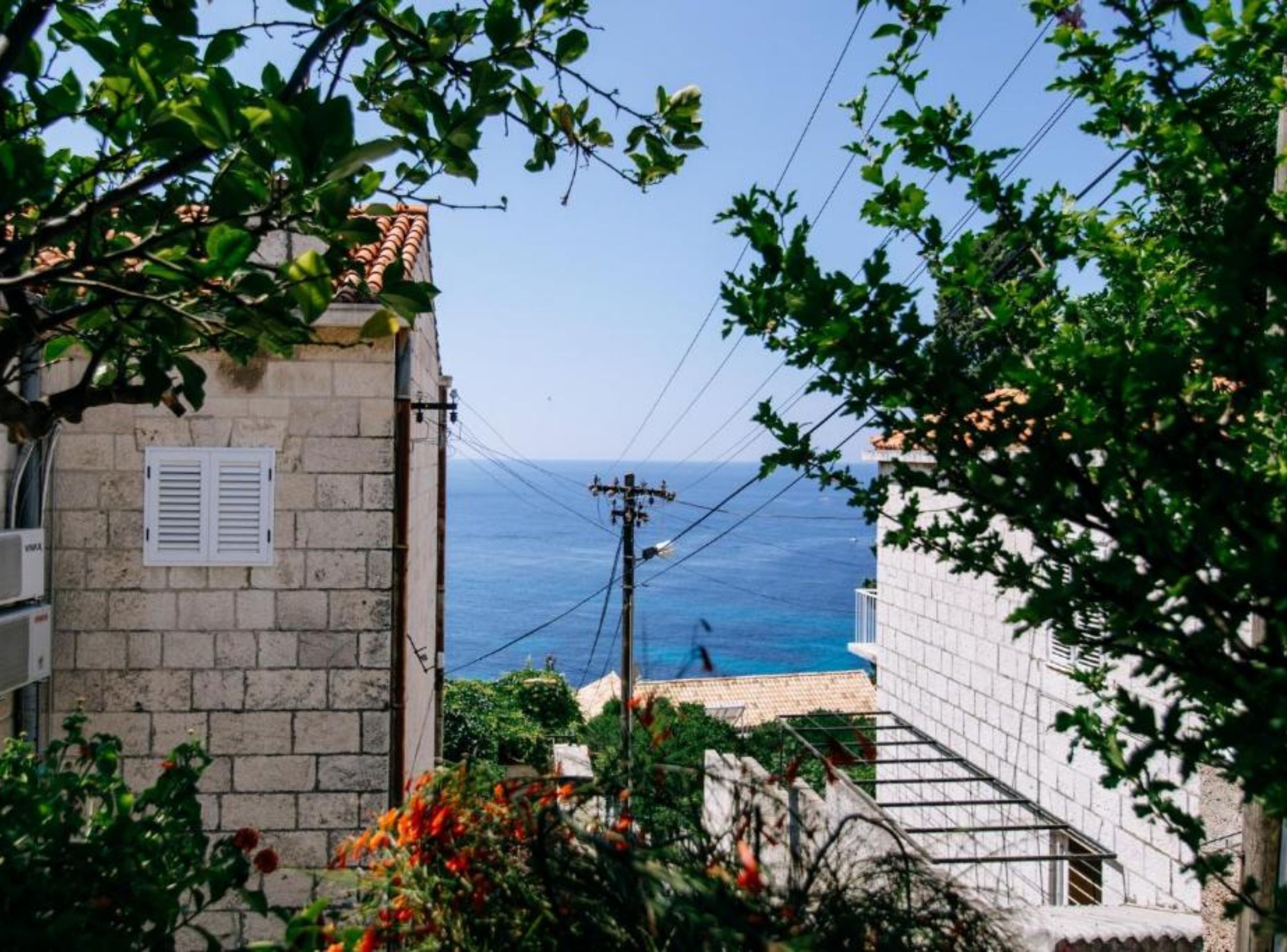 Une vue sur la côte, avec un bâtiment en pierre, un ciel dégagé et une personne qui se promène au bord de la mer.