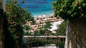 A coastal view with a beach, umbrellas, and lounge chairs. - Apartments Luce & Toma (Dubrovnik)