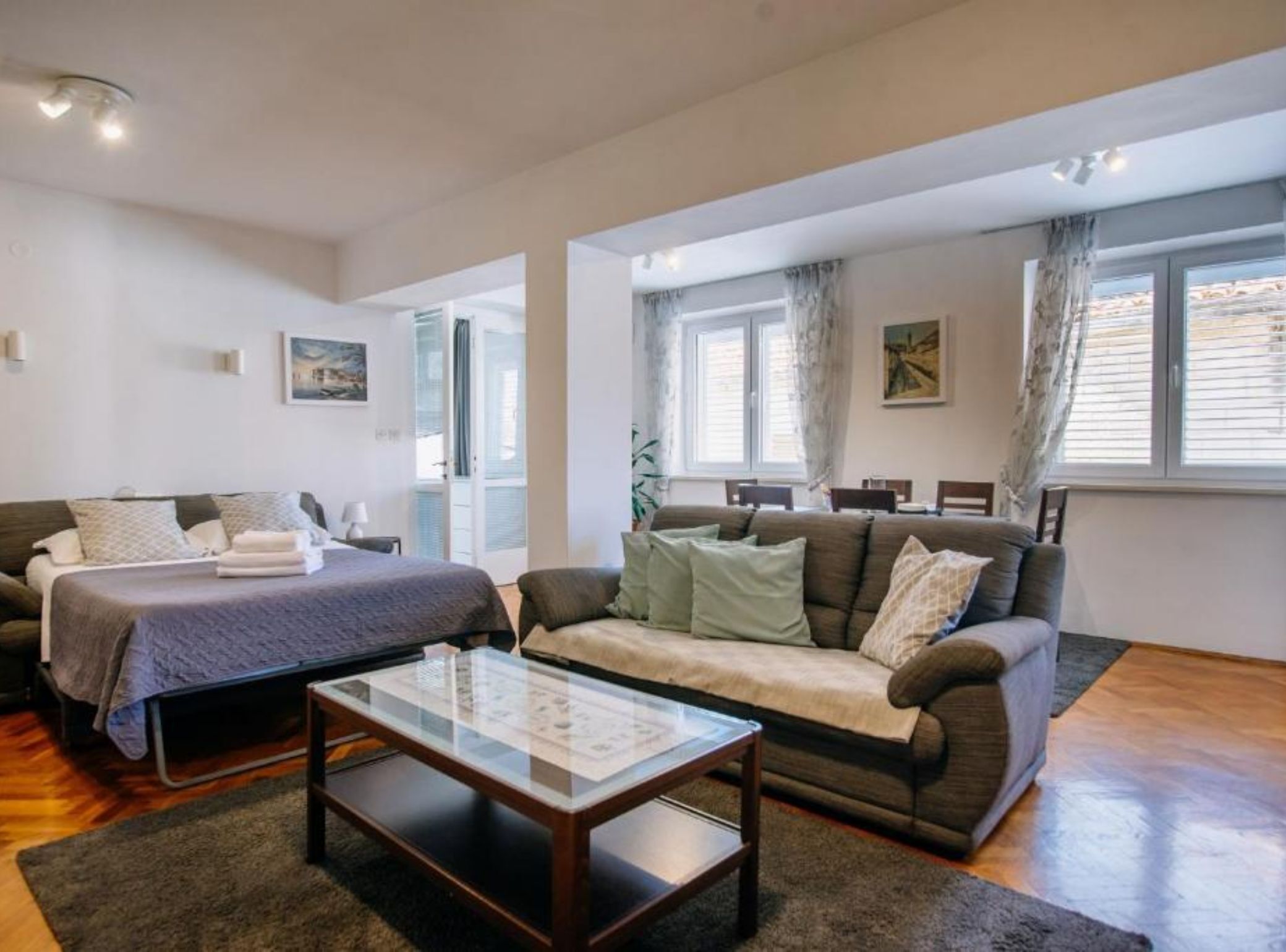 A modern living room with a bed, a sofa, and a glass coffee table.