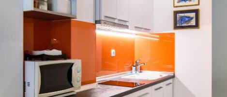 A modern kitchen with white cabinets, an orange accent wall, a microwave, and a sink.