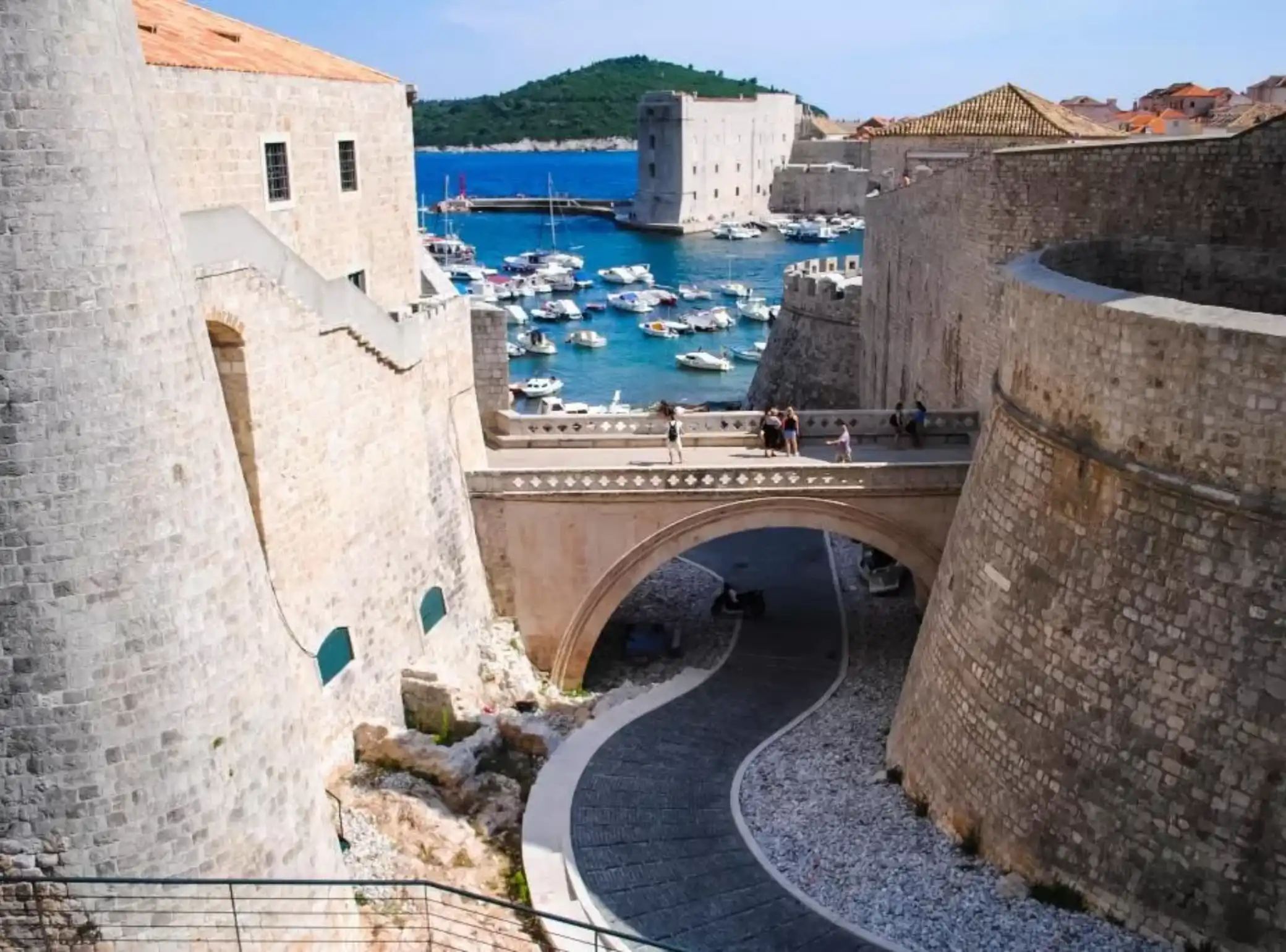 A historic stone bridge connecting two parts of a fortified town with a marina full of boats in the background.
