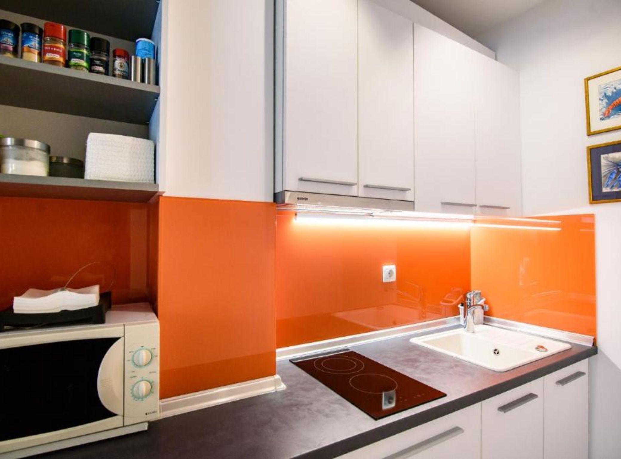 Une cuisine moderne avec des meubles blancs, un micro-ondes noir et un pare-feu orange.
