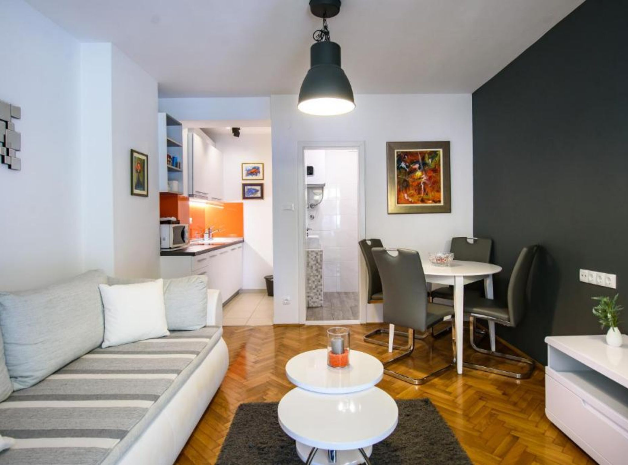 Ein modernes Wohnzimmer mit einer Couch, zwei runden Tischen, einem Essbereich mit Stühlen und einer Küche im Hintergrund.