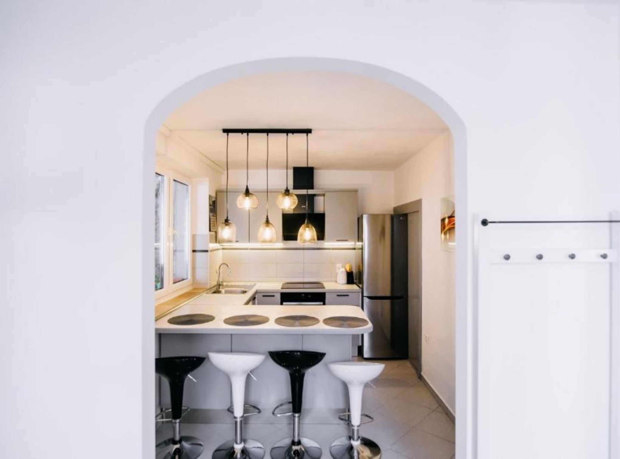A modern kitchen with a central island, pendant lights, and bar stools.