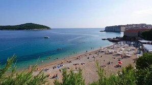 A beach with clear blue water, a small boat, and a historic building on the right. - Apartments Luce & Toma (Dubrovnik)