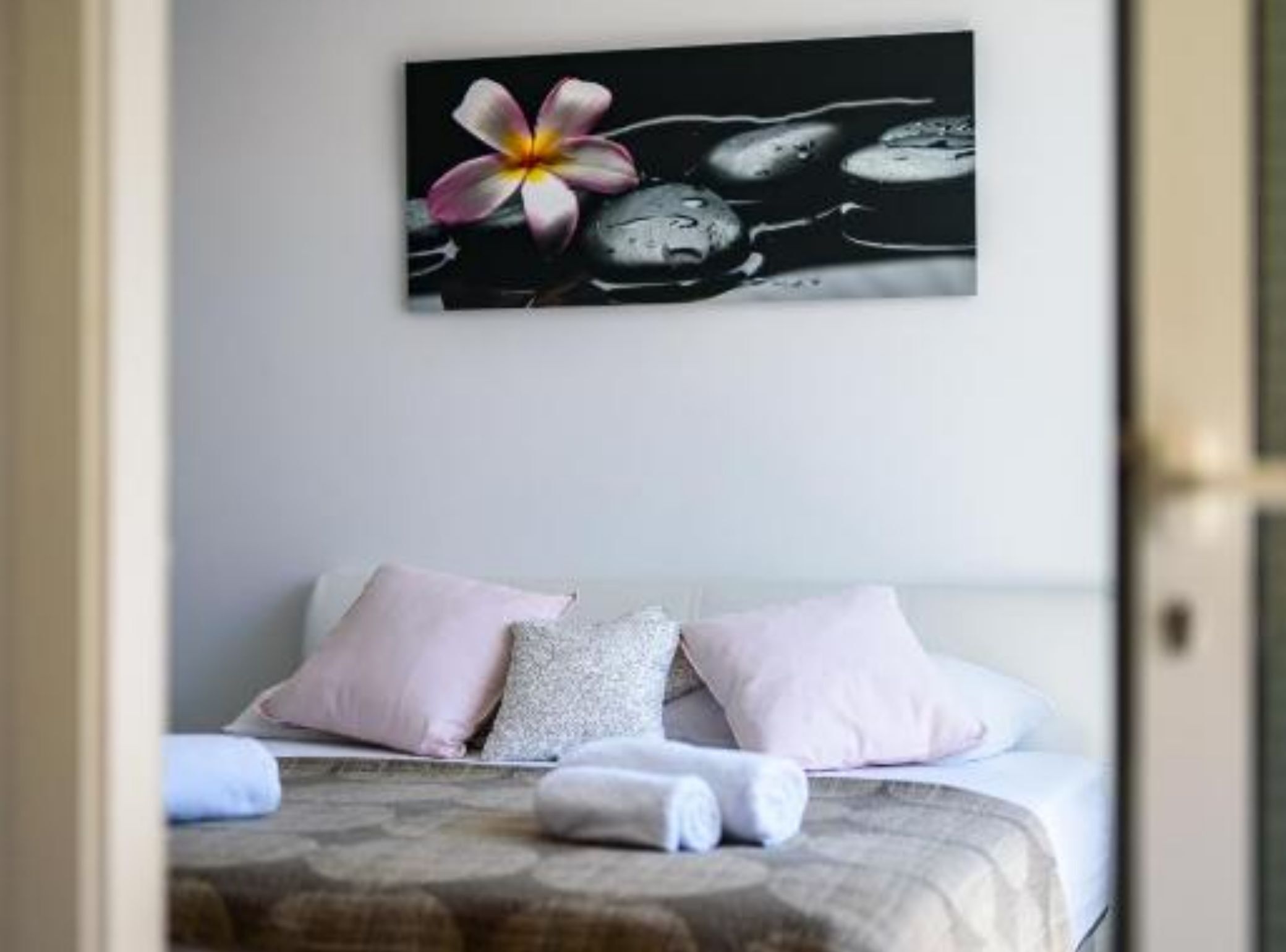 A bedroom with a bed, pillows, and a wall-mounted artwork of a flower and stones.