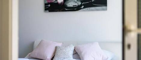 A bedroom with a bed, pillows, and a wall-mounted artwork of a flower and stones.