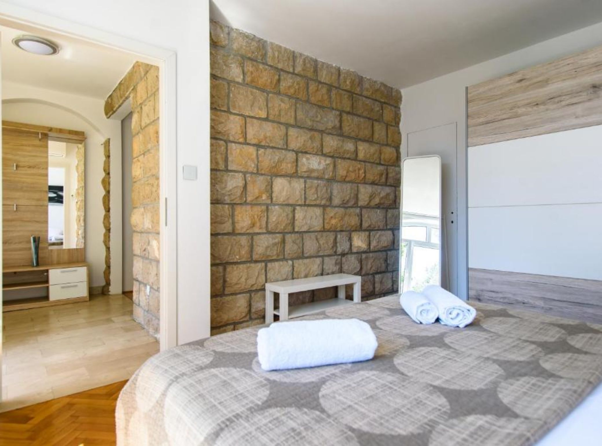 Une chambre avec un mur en pierre, un banc en bois, un lit avec des serviettes pliées et un miroir.