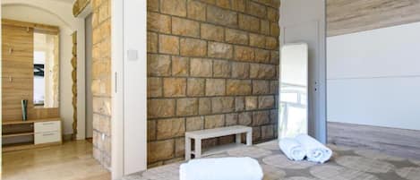 Une chambre avec un mur en pierre, un banc en bois, un lit avec des serviettes pliées et un miroir.