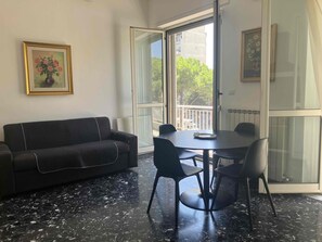 A room with a dark sofa, a round table with chairs, a large window, and a framed picture on the wall. - B&B mare mio - the warmth of home (Pescara)
