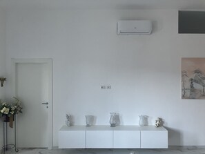A minimalist room with a white console table displaying several vases, a door, and a wall-mounted air conditioner. - B&B mare mio - the warmth of home (Pescara)