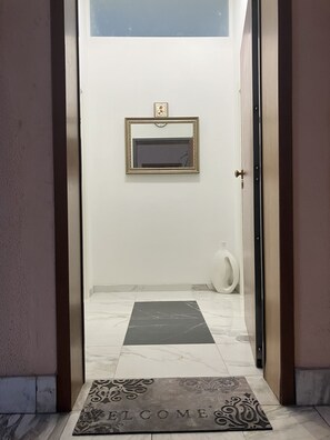 Un hall d’entrée propre et moderne, avec un sol en marbre, un paillasson et un tableau encadré au mur.