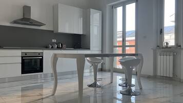 Une cuisine moderne avec des meubles blancs, une hotte en acier inoxydable et une grande fenêtre qui laisse entrer la lumière naturelle.