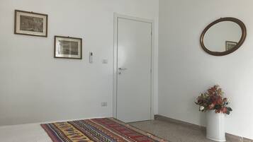 Ein Schlafzimmer mit einem Bett, einer Tür, zwei gerahmten Bildern, einem wandmontierten Spiegel und einer Vase mit Blumen.