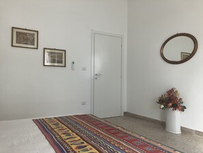 Une chambre à coucher comprenant un lit, une porte, deux tableaux encadrés, un miroir fixé au mur et un vase avec des fleurs.