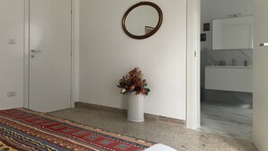 A bedroom with a bed, a white door, a wall-mounted mirror, and a bathroom visible through an open door.