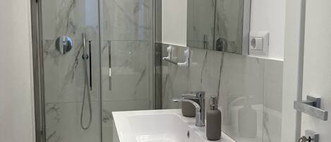Une salle de bain moderne avec une douche à parois de verre, un meuble-lavabo blanc et un grand miroir.
