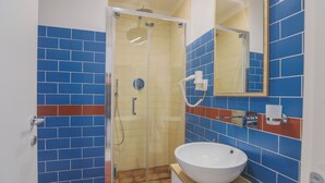 Een badkamer met een douchecabine van glas, een witte wastafel en blauw-rode betegelde muren.