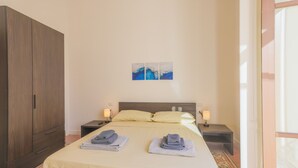 Een net opgemaakt bed met twee handdoeken, een houten kledingkast, nachtkastjes met lampen, en een kunstwerk aan de muur.