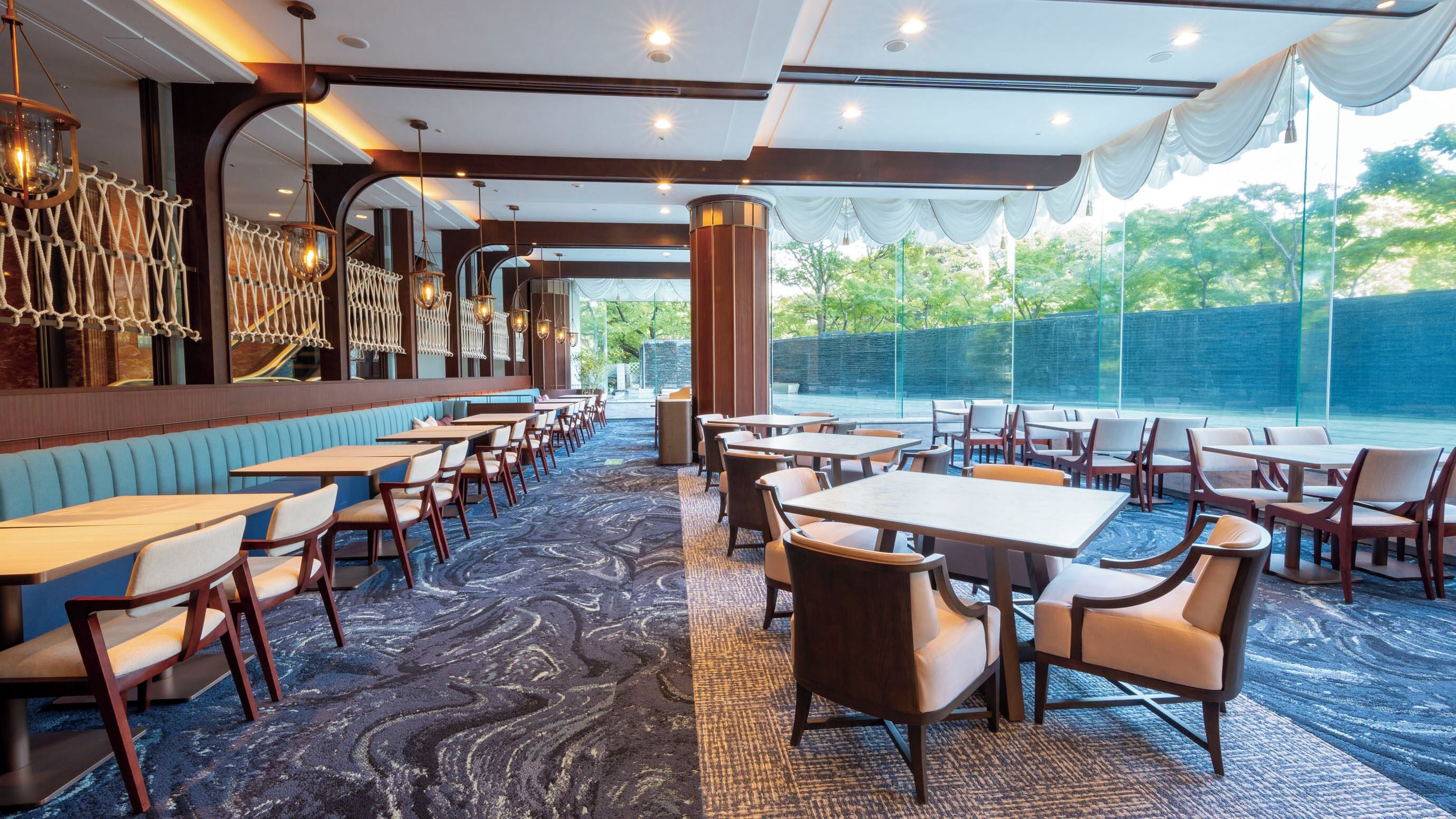 A restaurant with a mix of booth and table seating, a patterned carpet, and a view of greenery outside.