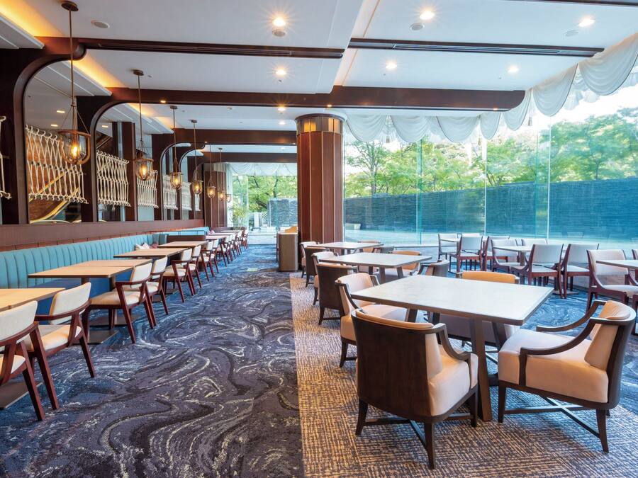 A restaurant with a mix of booth and table seating, a patterned carpet, and a view of greenery outside.