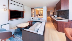 Quarto de hotel moderno com sofá, televisão, área de refeições e cozinha.