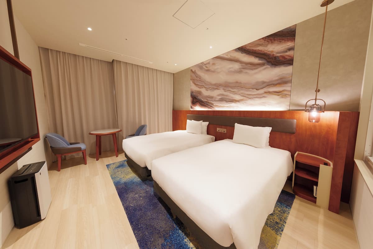 Ein Hotelzimmer mit zwei Betten, einem Schreibtisch, einem Stuhl und einer großen Wandmalerei.