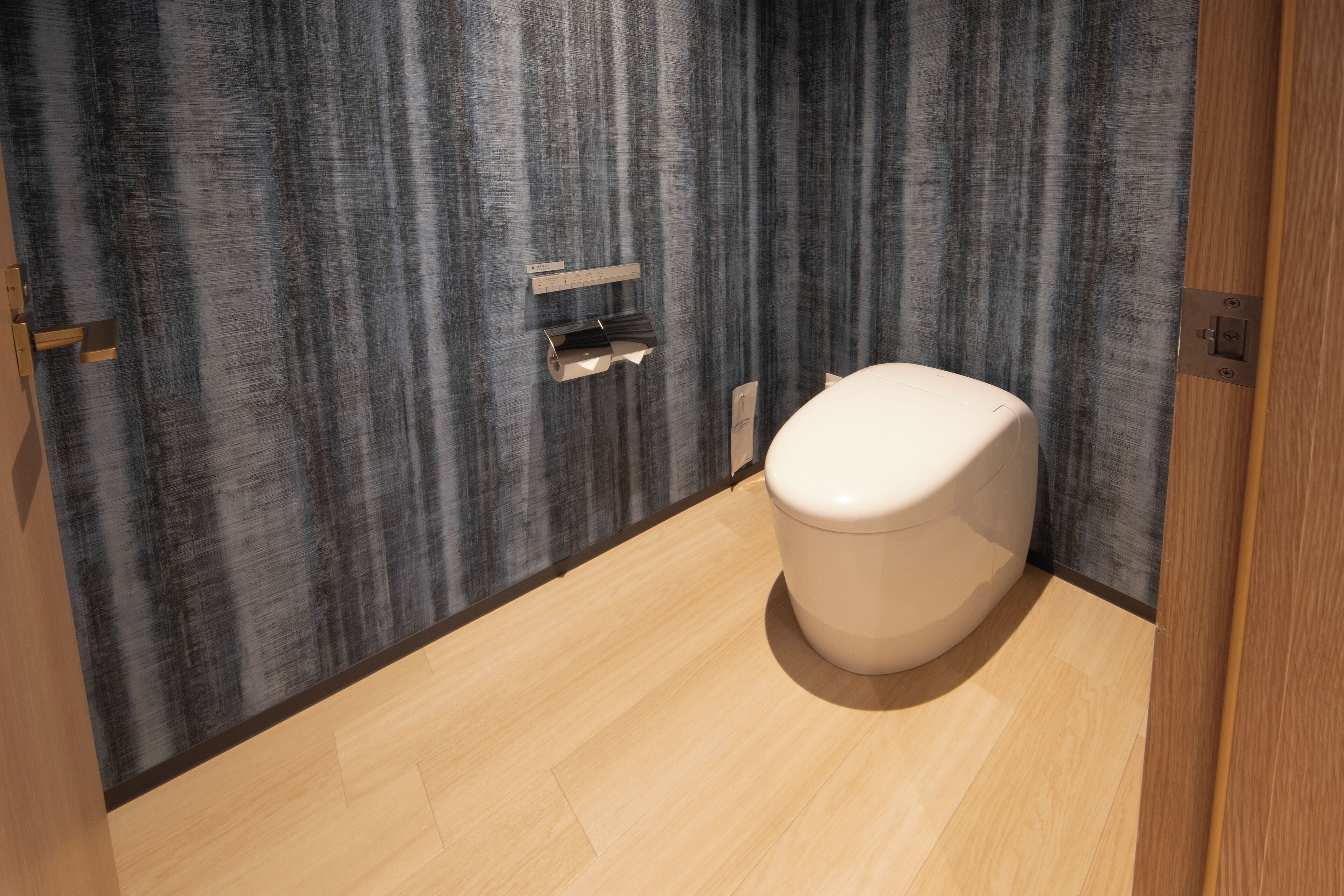 Un baño moderno con suelo de madera, inodoro blanco y pared con textura.