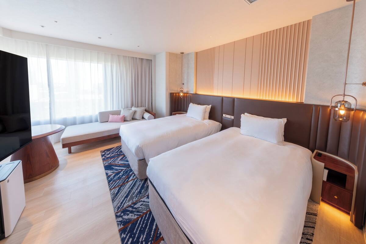 Ein Hotelzimmer mit zwei Betten, einer Sitzecke, einem Fernseher und einer Minibar.
