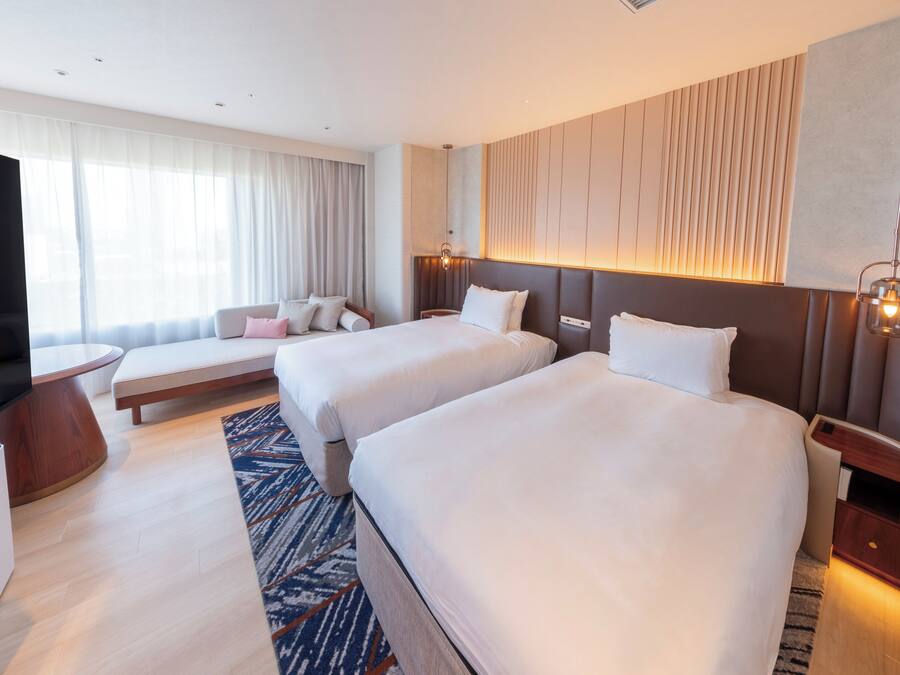 A hotel room with two beds, a seating area, a TV, and a minibar.