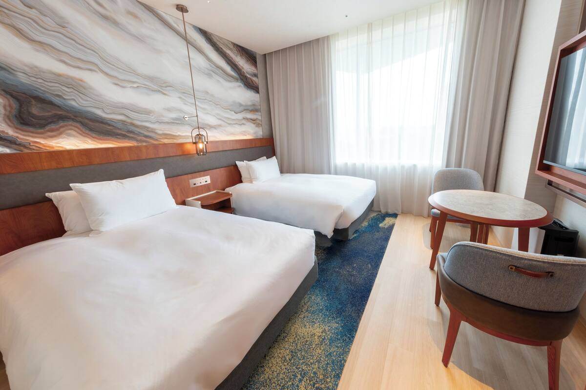 Ein Hotelzimmer mit zwei Betten, einem kleinen Tisch, einem Stuhl, einem Fernseher und einer Marmorwand.