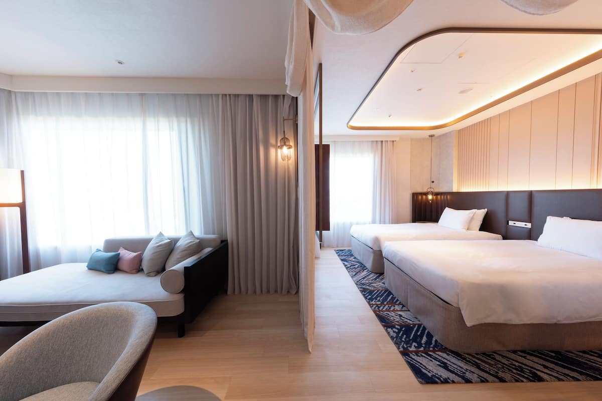 Ein modernes Hotelzimmer mit einer Couch, zwei Betten, einem Sessel und einem gemusterten Teppich.
