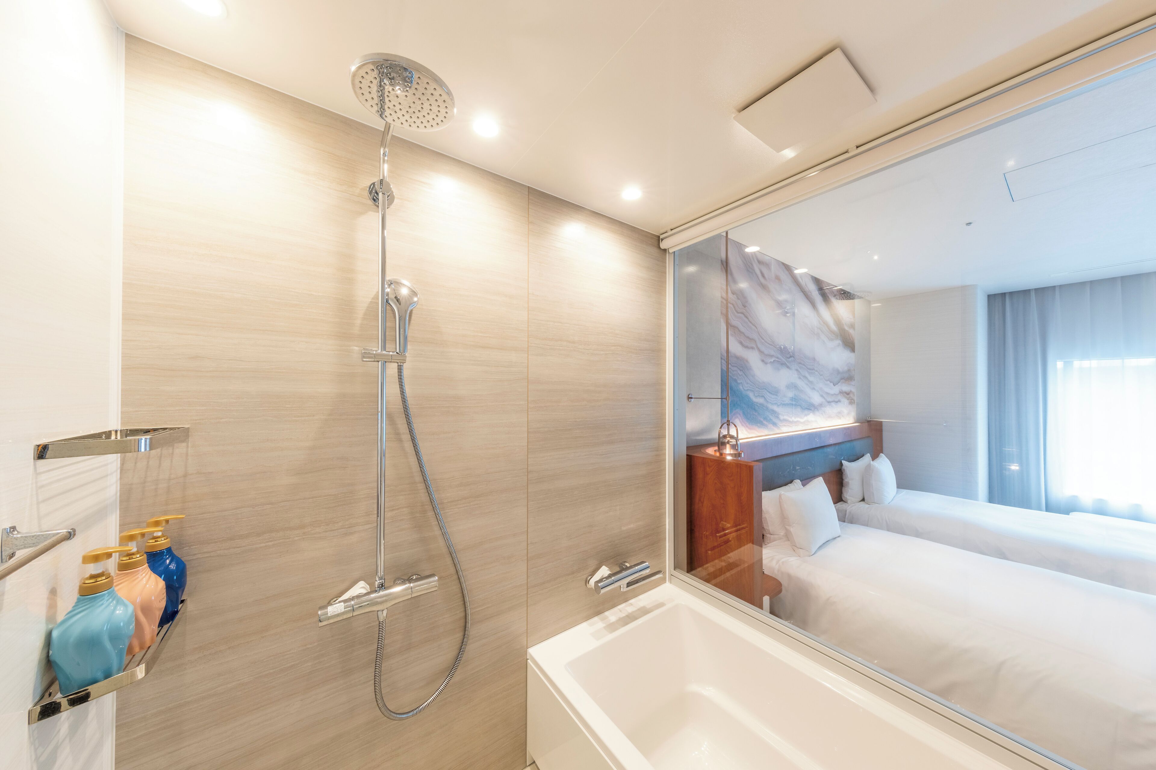 Un bagno moderno con vasca, doccia e un grande specchio che riflette una camera da letto con un letto e un comodino.