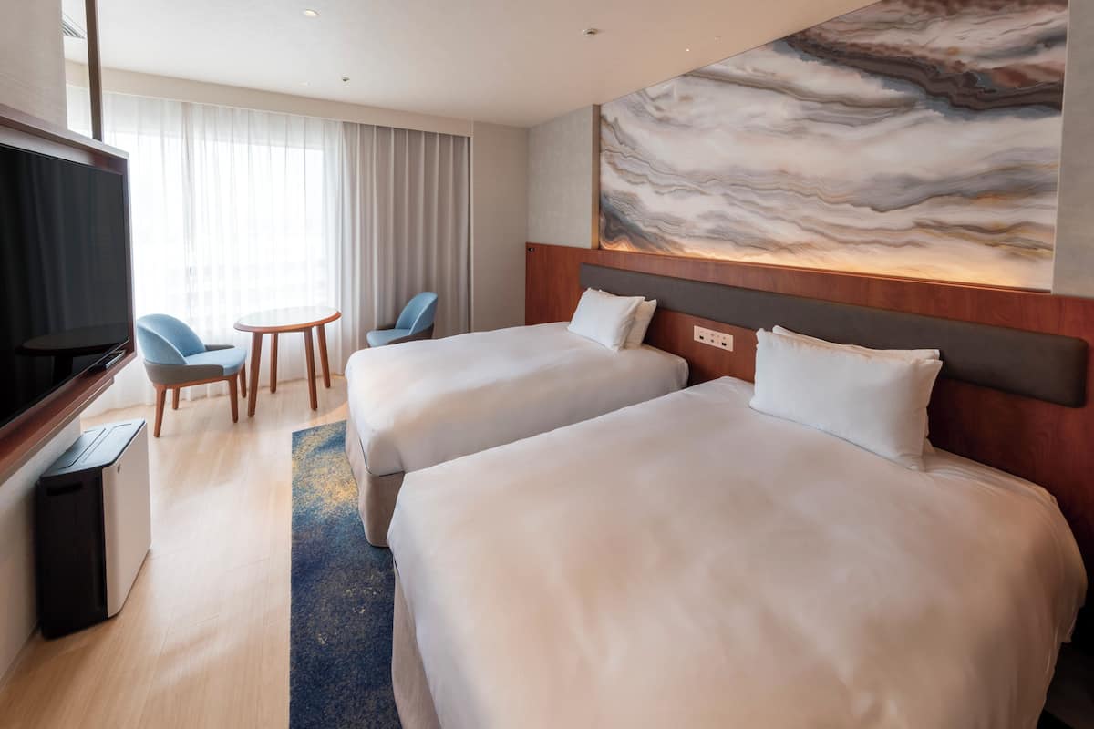 Ein Hotelzimmer mit zwei Betten, einem Fernseher, einem Schreibtisch und einem Stuhl.